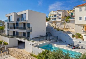 A modern multi-story building with a swimming pool, balconies, and a staircase leading to upper levels. - Apartments Penthouse Lux (Rogoznica)