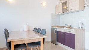 A modern kitchen with a dining table, chairs, a refrigerator, and cabinets. - Apartment Adriatic Panorama (Podstrana)