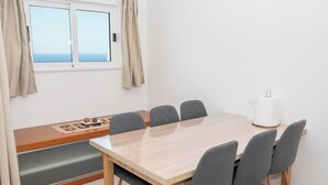 A room with a wooden table, six grey chairs, a bench with a cushion, a window with curtains, and a white lamp. - Apartment Adriatic Panorama (Podstrana)