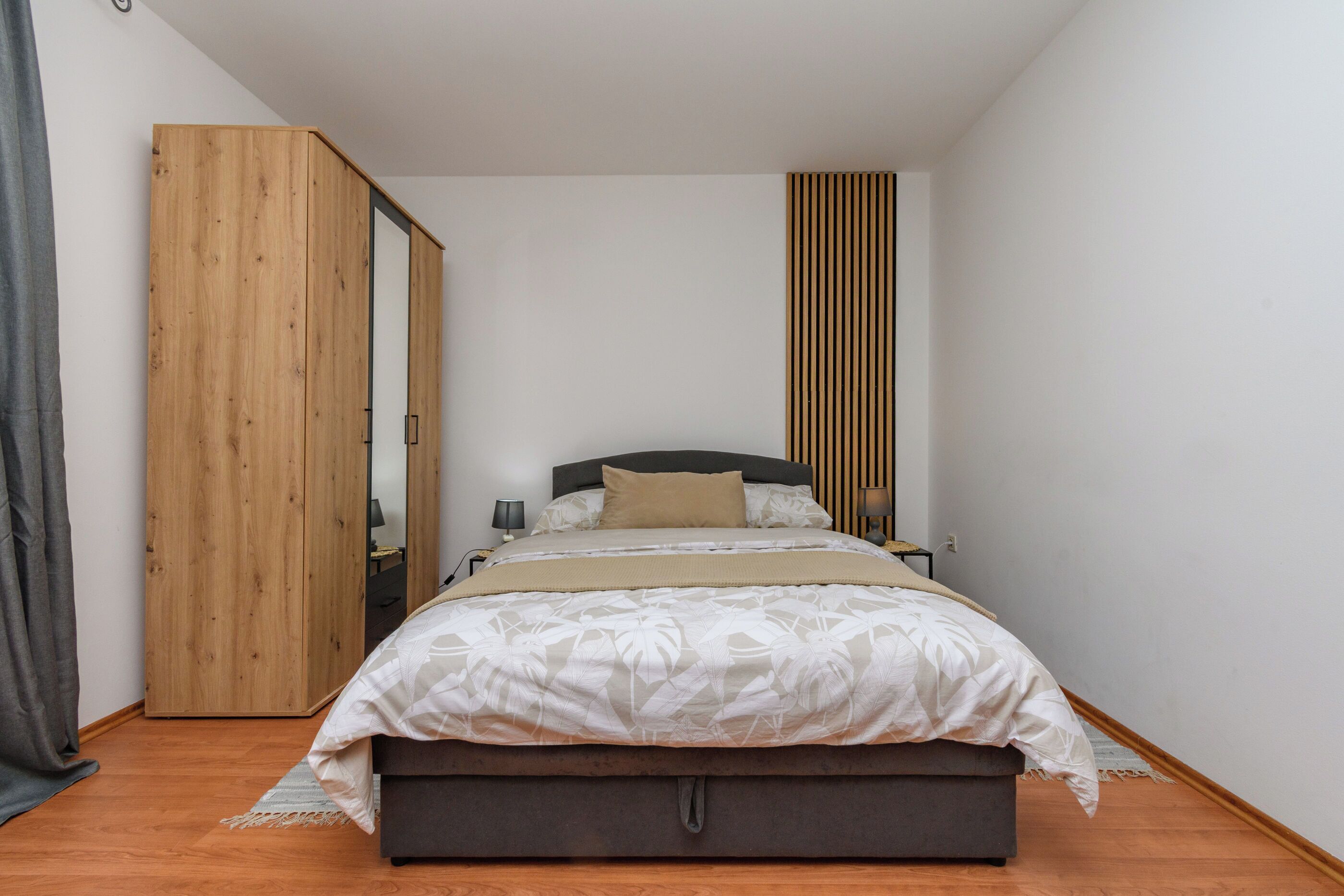 A bedroom with a bed, a wooden wardrobe, a bedside table, and a nightstand.