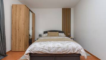 A bedroom with a bed, a wooden wardrobe, a bedside table, and a nightstand.