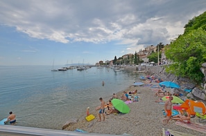 A pebbled beach with people sunbathing, swimming, and walking along the shore. - Apartment Nature (Klana)
