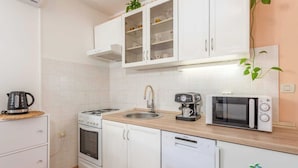 A compact kitchen with white cabinets, a gas stove, a microwave, and a coffee maker. - Apartment Nature (Klana)