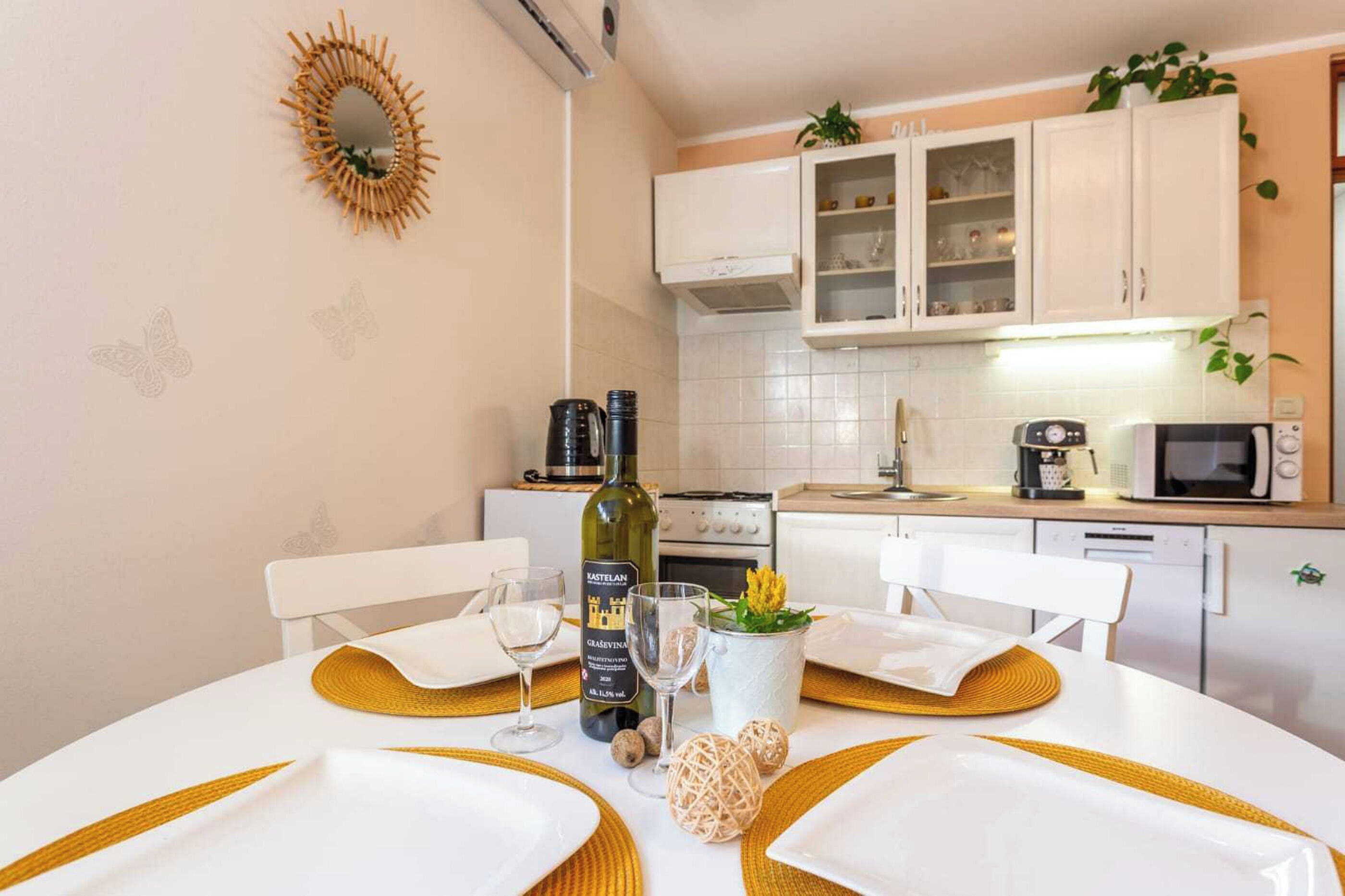 A dining area with a table set for two, a bottle of wine, and a microwave in the background.