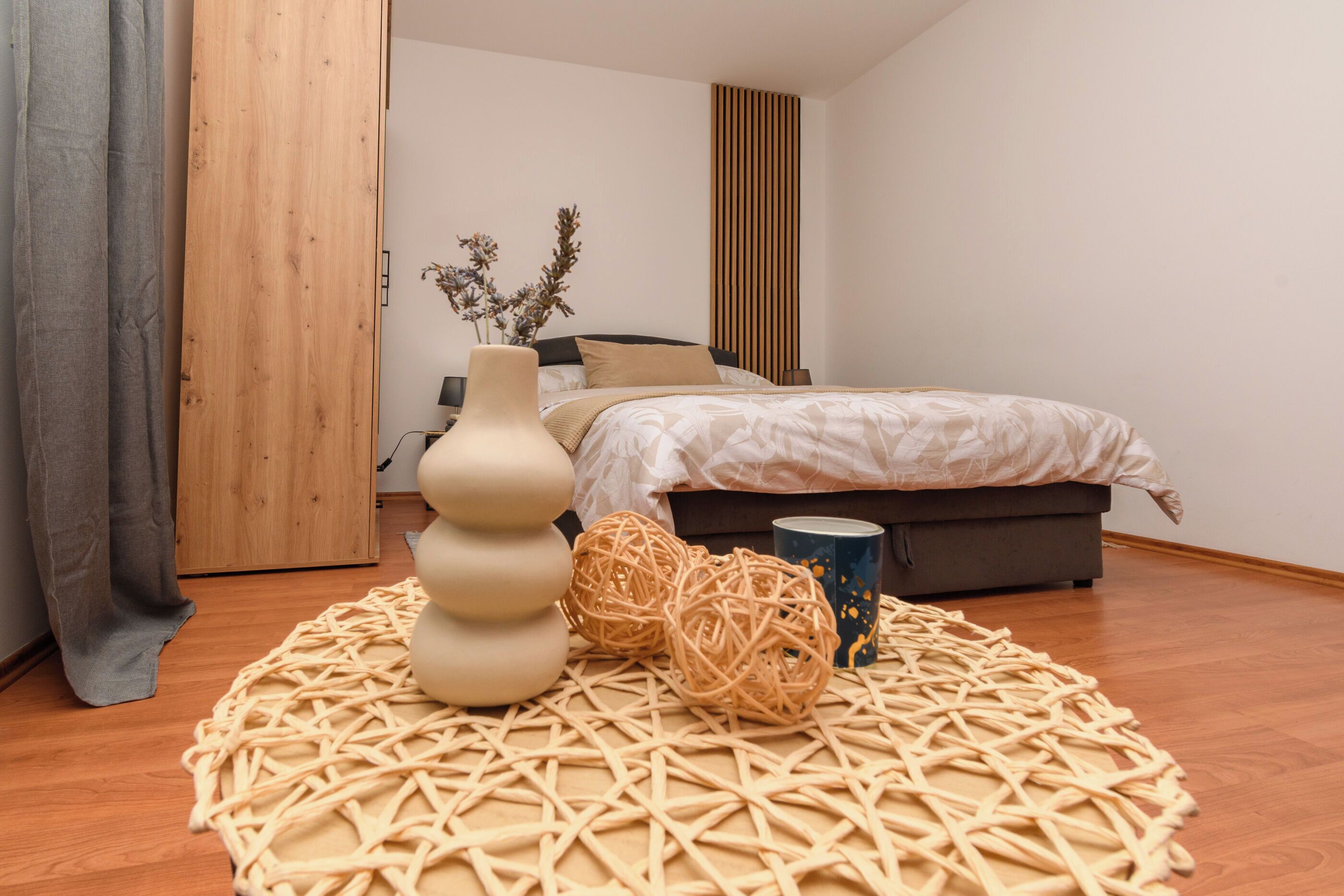 A bedroom with a bed, a bedside table, a vase, and a woven rug.