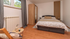 A bedroom with a bed, a chair, a table, a radiator, and a window. - Apartment Nature (Klana)