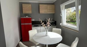 A compact kitchen with a red refrigerator, white chairs, and a dining table with a vase of flowers. - Apartments Casa Zanoff (Umag)