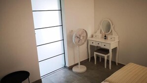 Ein Schlafzimmer mit weißem Schminktisch, einem Spiegel, einem Ventilator und einem Bett.