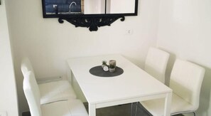 A small, white, square dining table with four white chairs, a black wall-mounted mirror above it, and a small potted plant on the table. - Apartments Casa Zanoff (Umag)