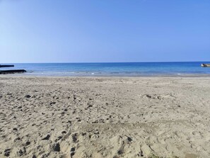 A sandy beach with footprints leading to the water, a pier on the left, and a clear blue sky. - Apartments Zanoff (Umag)