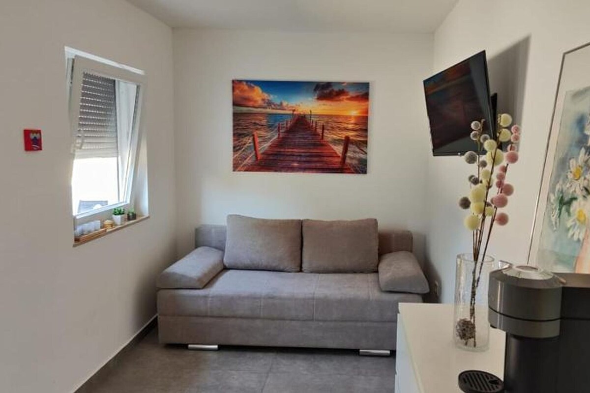 A modern living room with a sofa, a painting of a sunset, a vase with flowers, and a coffee machine.