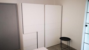 Ein Zimmer mit einer grauen Tür, einem weißen Kleiderschrank und einem schwarzen Hocker.