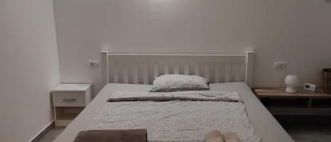 A neatly made bed with a white headboard, a bedside table with a lamp, and a small nightstand with a clock.