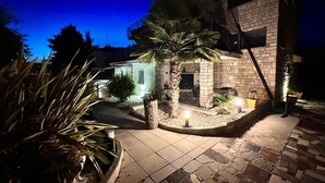 Ein Gebäude aus Stein mit einer Terrassenfläche, einer Palme und einer kleinen Sitzgelegenheit im Freien.