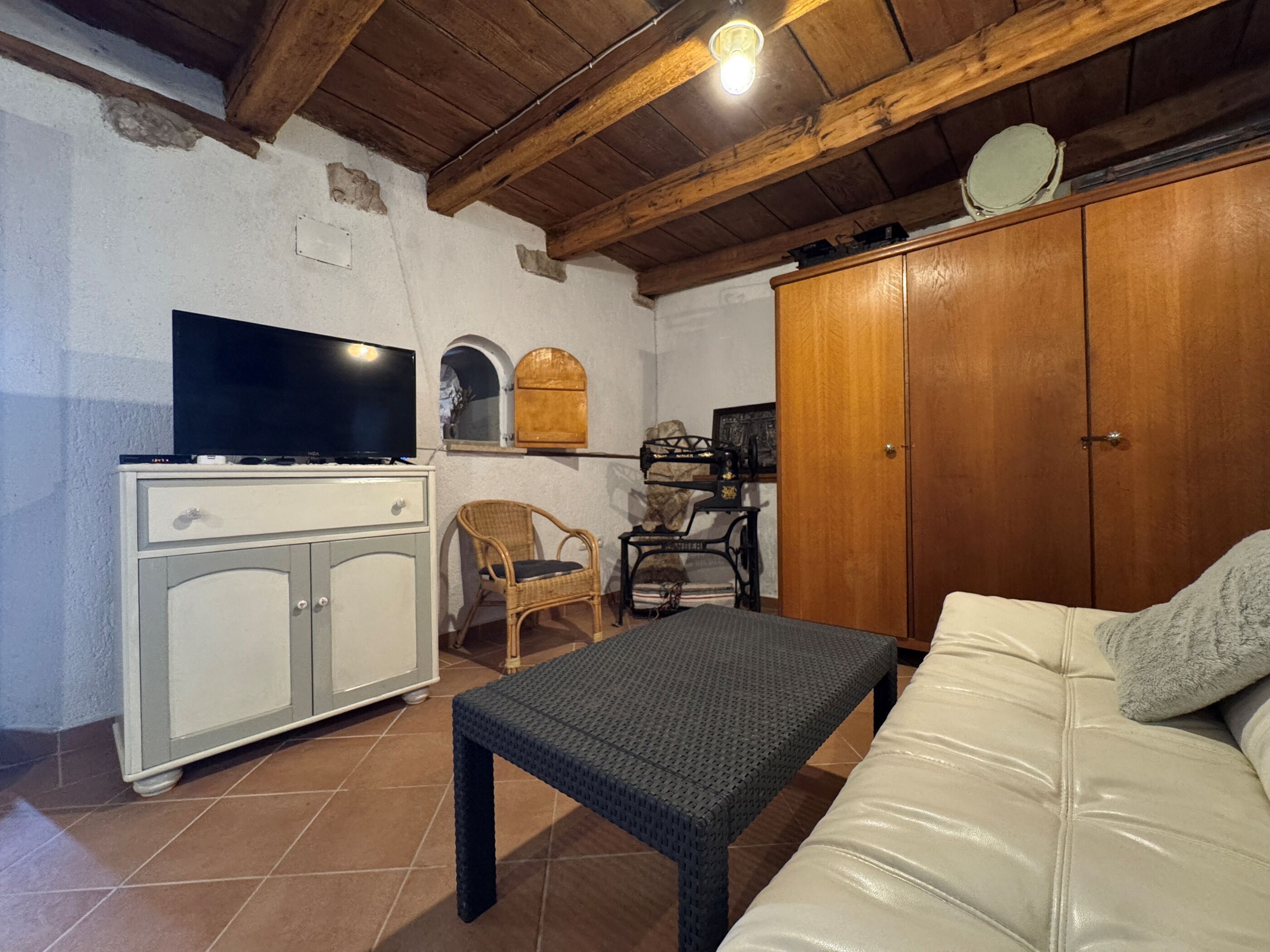 Una habitación con televisión sobre un mueble bajo, una silla de mimbre, un sofá y un armario de madera.