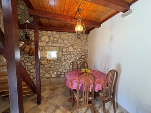 Ein Zimmer mit Steinwänden und Holzbalkendecke, ein Tisch mit rosa Tischdecke und eine Hängeleuchte.