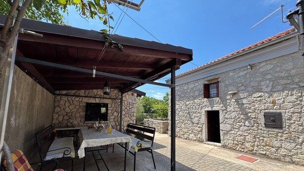 A stone building with a covered patio, a table with chairs, and a bench. - Apartment Prelec (Crikvenica)