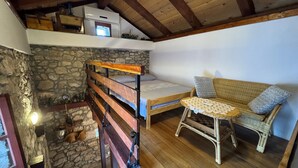 A rustic room with a loft bed, a wicker sofa, a small table, and a stone wall. - Apartment Prelec (Crikvenica)