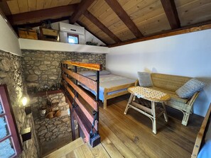 Ein rustikaler Raum mit Schlafkoje, einem Korbsessel, einem kleinen Tisch und einer Steinwand.