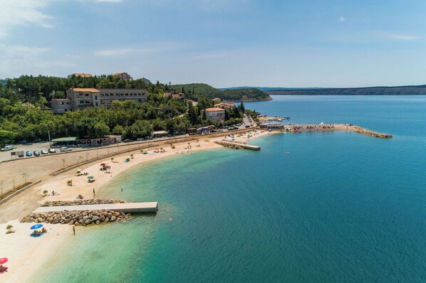 Un pueblo costero con una playa, aguas claras y edificios en una colina.