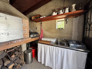 Una cocina rústica con un horno de ladrillo, estufa a gas, un lavaplatos y un ventanal pequeño.