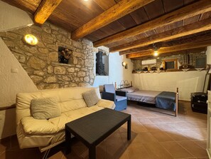 A cozy room with a stone wall, a wooden ceiling, a sofa, a small table, and a bed. - Apartment Prelec (Crikvenica)