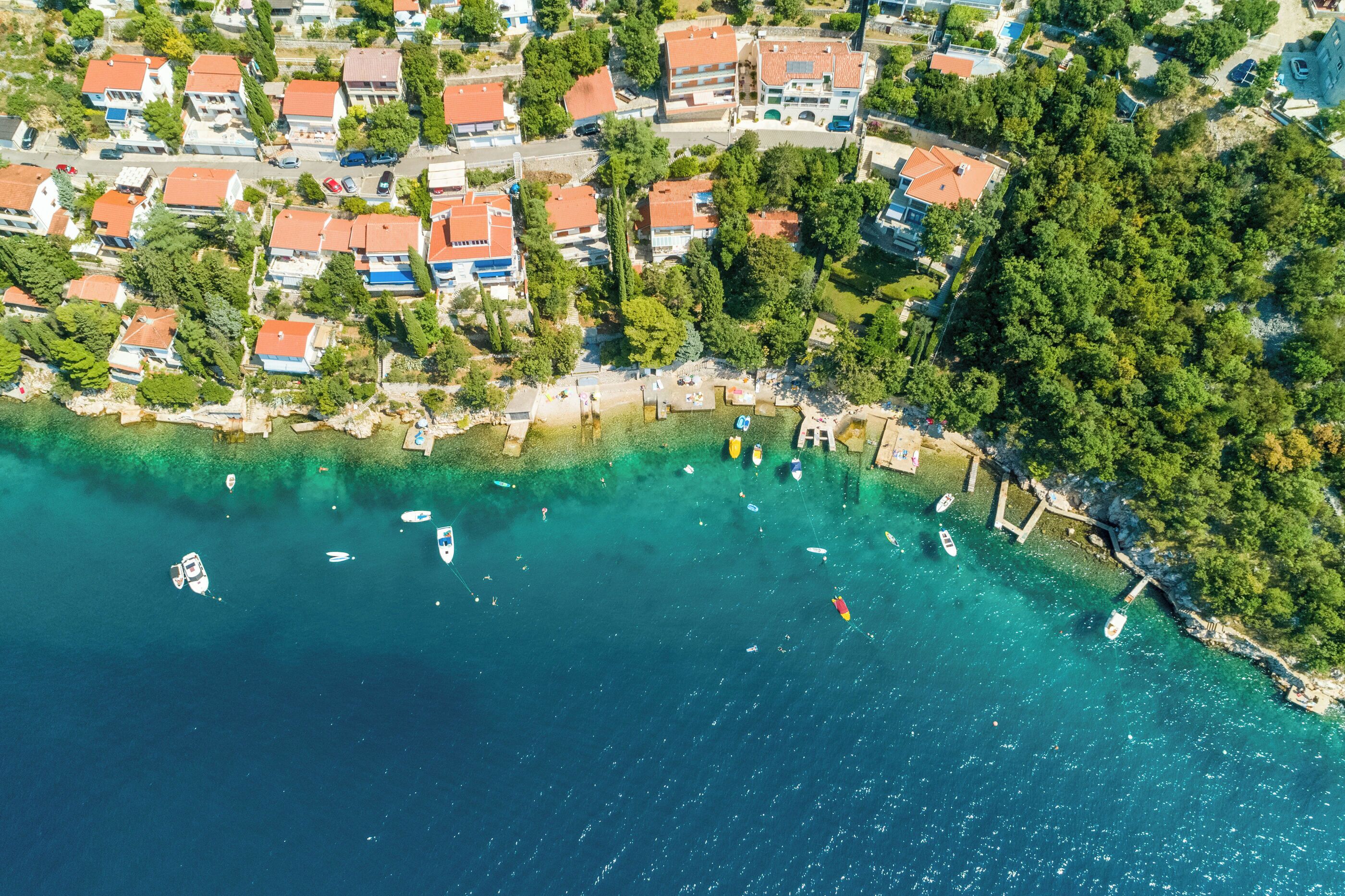 An aerial view of a coastal residential area with houses, a beach, and boats.