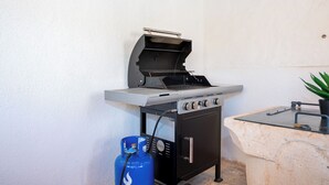 Una griglia barbecue con bombola del gas, un piano di lavoro in pietra e una pianta in vaso.