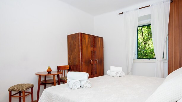 Una camera da letto con un letto, un armadio in legno, un tavolino con un vaso e una sedia.