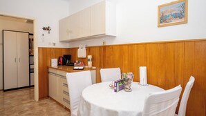 Un'area pranzo con un tavolo rotondo, sedie bianche, un quadro appeso alla parete e una cucina sullo sfondo.