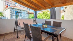 Patio esterno con tavolo e sedie, una lampada a sospensione e vista su un edificio in pietra.