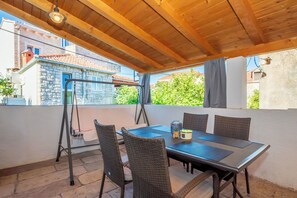 Eine Terrasse im Freien mit Tisch und Stühlen, einer hängenden Leuchte und Blick auf ein Steinhaus.