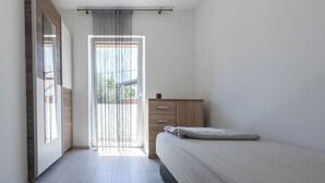 A bedroom with a bed, a wooden wardrobe, a window with curtains, and a door. - House Danijel (Novi Vinodolski)