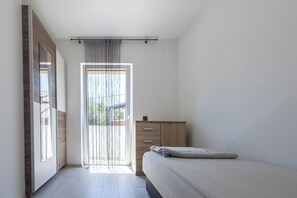 A bedroom with a bed, a wooden wardrobe, a window with curtains, and a door. - House Danijel (Novi Vinodolski)