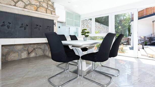 A modern kitchen with stone accents, a dining area with black chairs, and a view of the outdoors. - House Danijel (Novi Vinodolski)