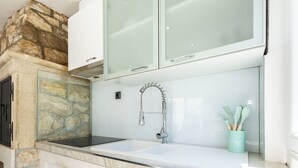 A bathroom with a stone accent wall, a white sink, a modern faucet, and a green cup with brushes. - House Danijel (Novi Vinodolski)