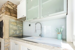 A bathroom with a stone accent wall, a white sink, a modern faucet, and a green cup with brushes. - House Danijel (Novi Vinodolski)
