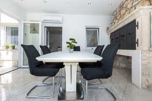 Een moderne eetruimte met een witte tafel, zwarte stoelen, een potplant en een stenen openhaard.