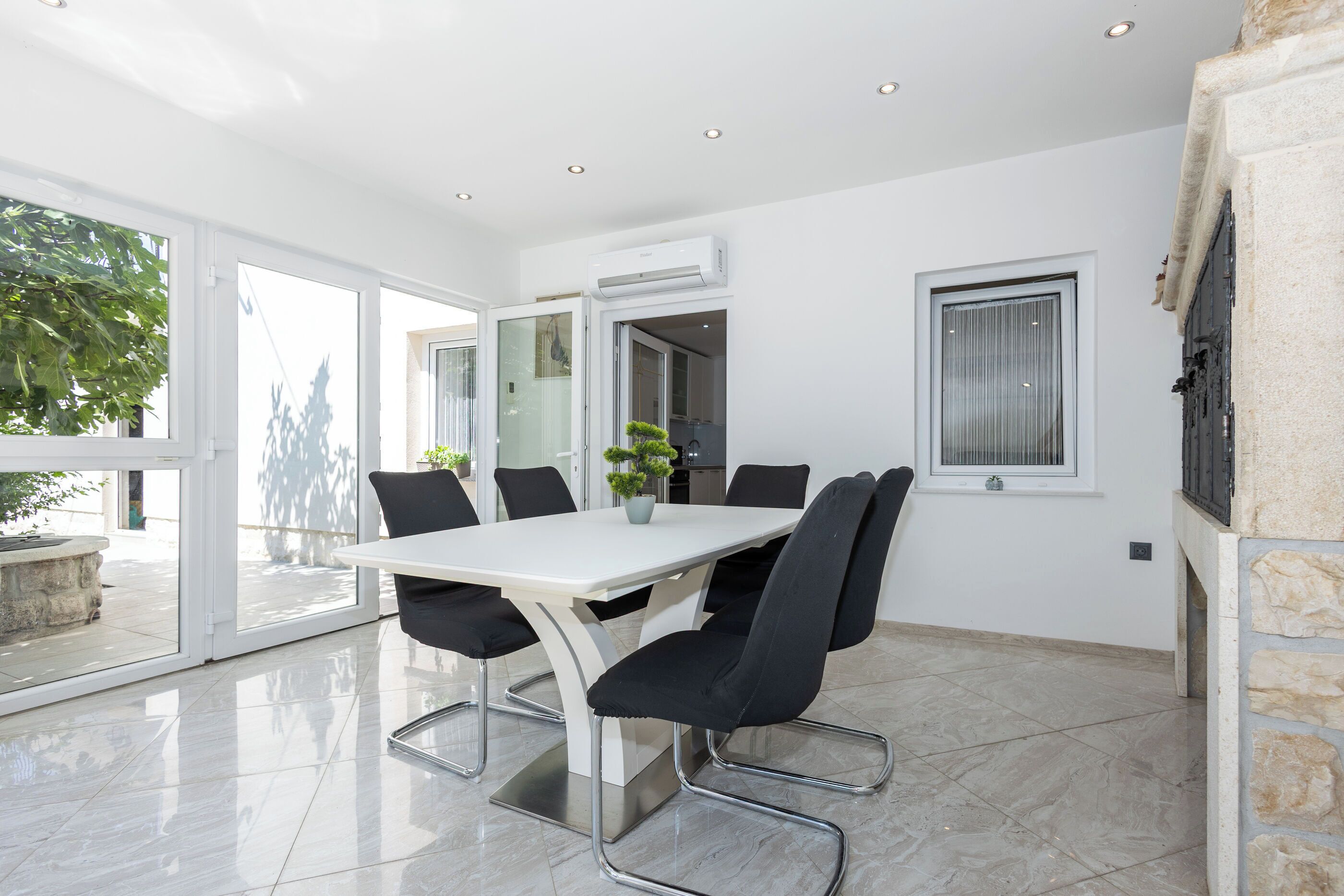 A modern dining area with a white table, black chairs, and a potted plant.