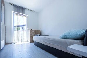 Een minimalistische slaapkamer met een bed, een houten nachtkastje en een schuifdeur naar een buitenruimte.