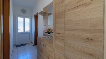 A hallway with a wooden wardrobe, a mirror, a clock on the wall, and a door with a window.