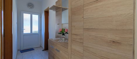 A hallway with a wooden wardrobe, a mirror, a clock on the wall, and a door with a window.