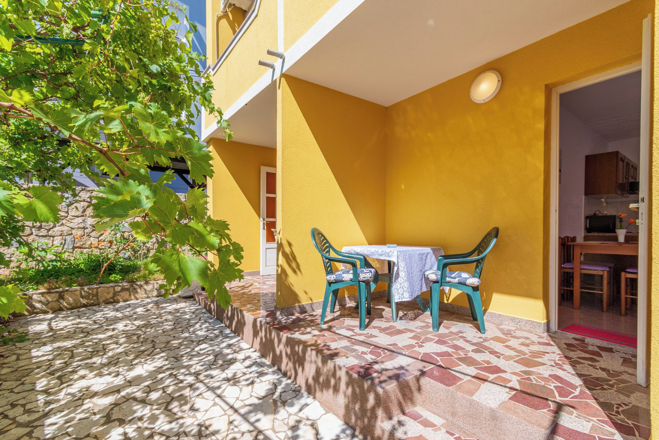 Une terrasse avec une table et des chaises, un sol en pierre et un mur jaune.