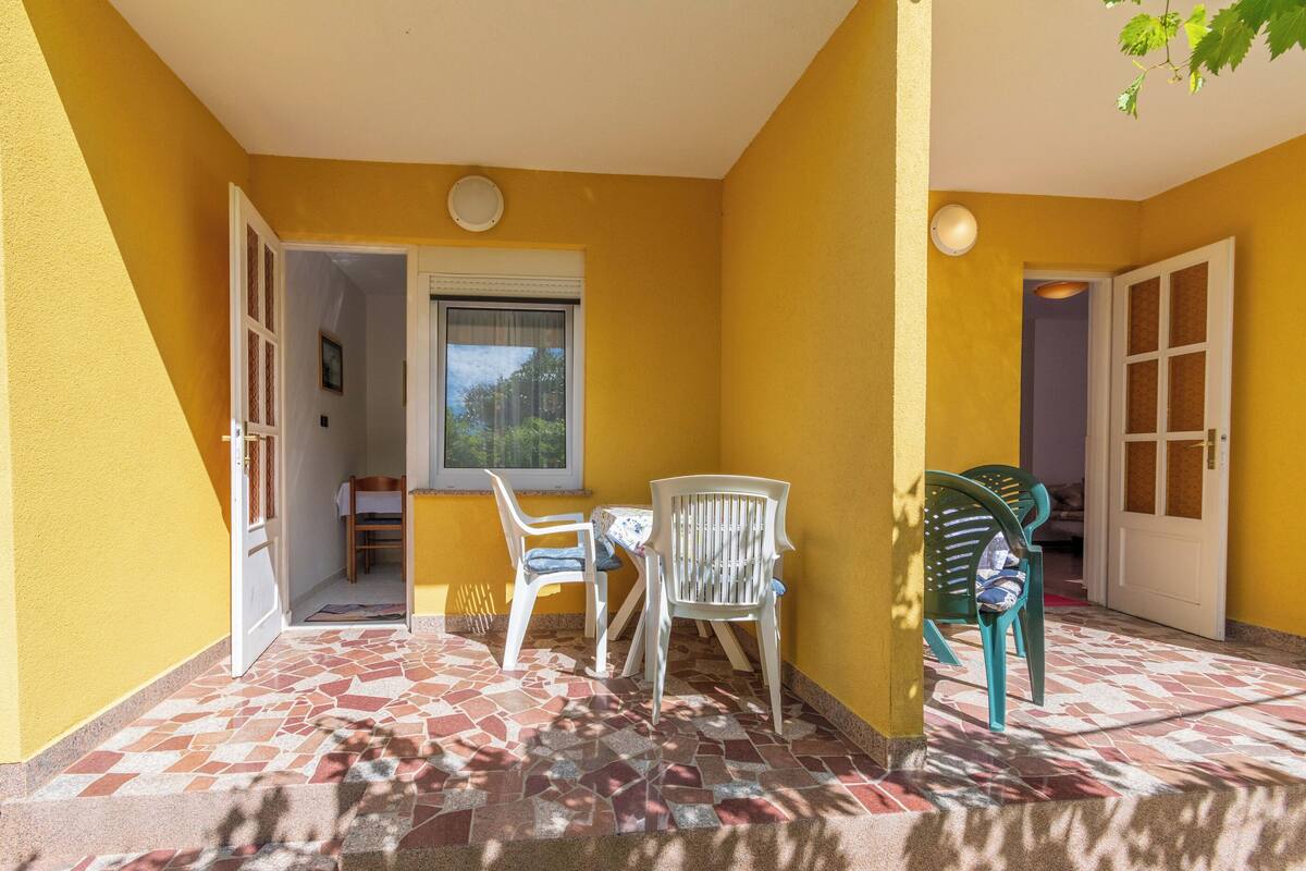 Ein gelbes Zimmer mit Fliesenboden, einem Fenster, einer Tür und zwei Stühlen.