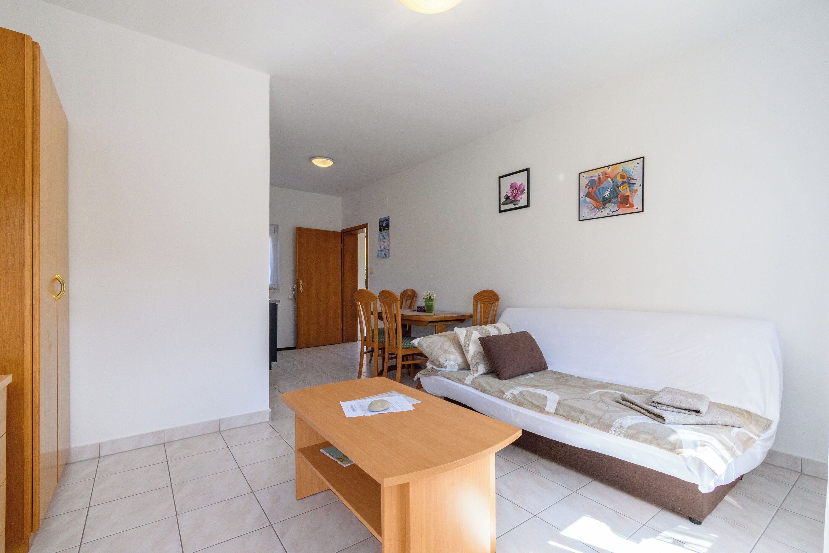 Una habitación con una cama, una mesa de madera, un comedor con sillas y una kitchenette al fondo.