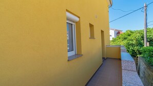 Un edificio amarillo con una ventana pequeña y una puerta, un camino de baldosas y un muro de piedra.