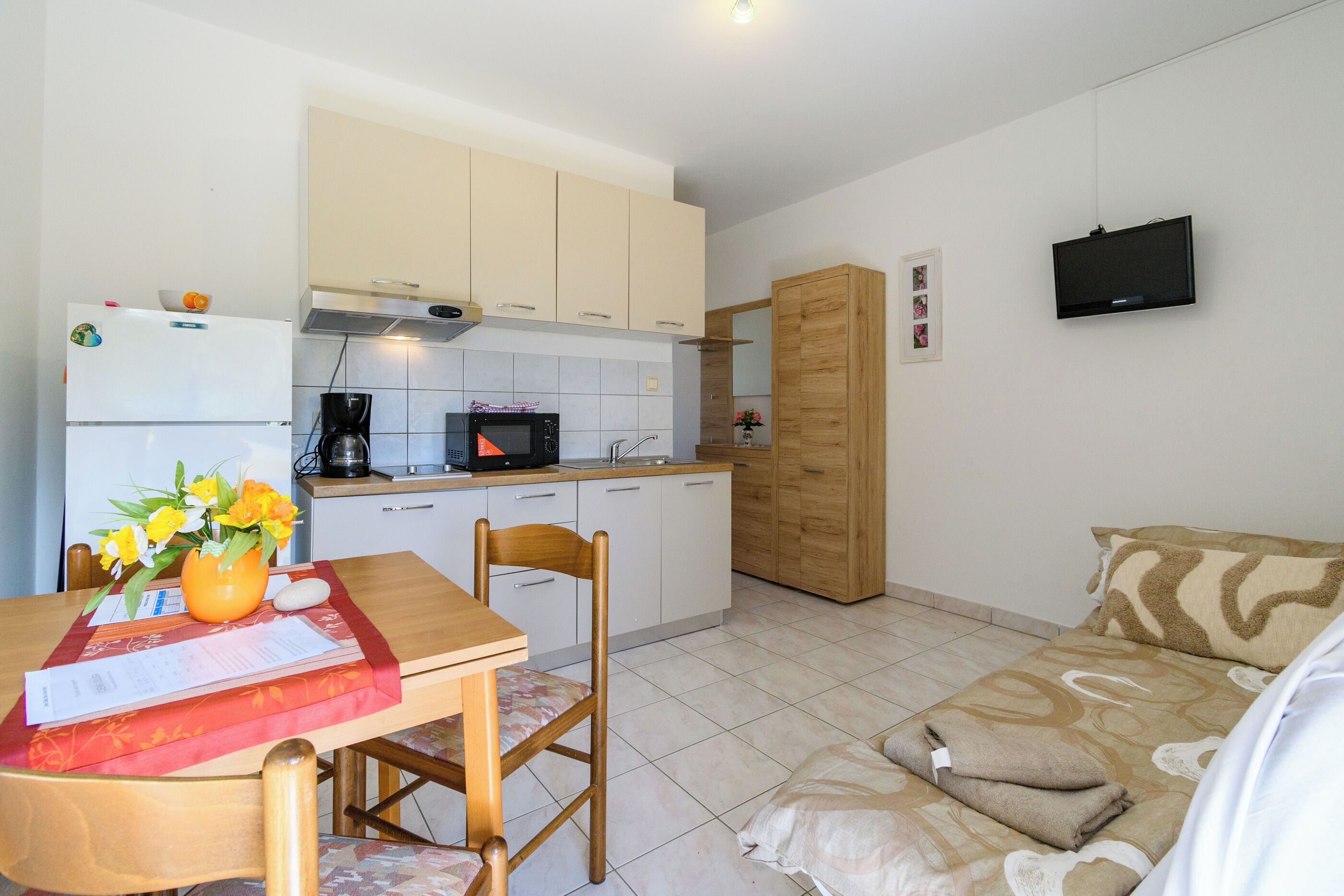 A compact living space with a kitchenette, a dining area with a table and chairs, a sofa, and a television mounted on the wall.