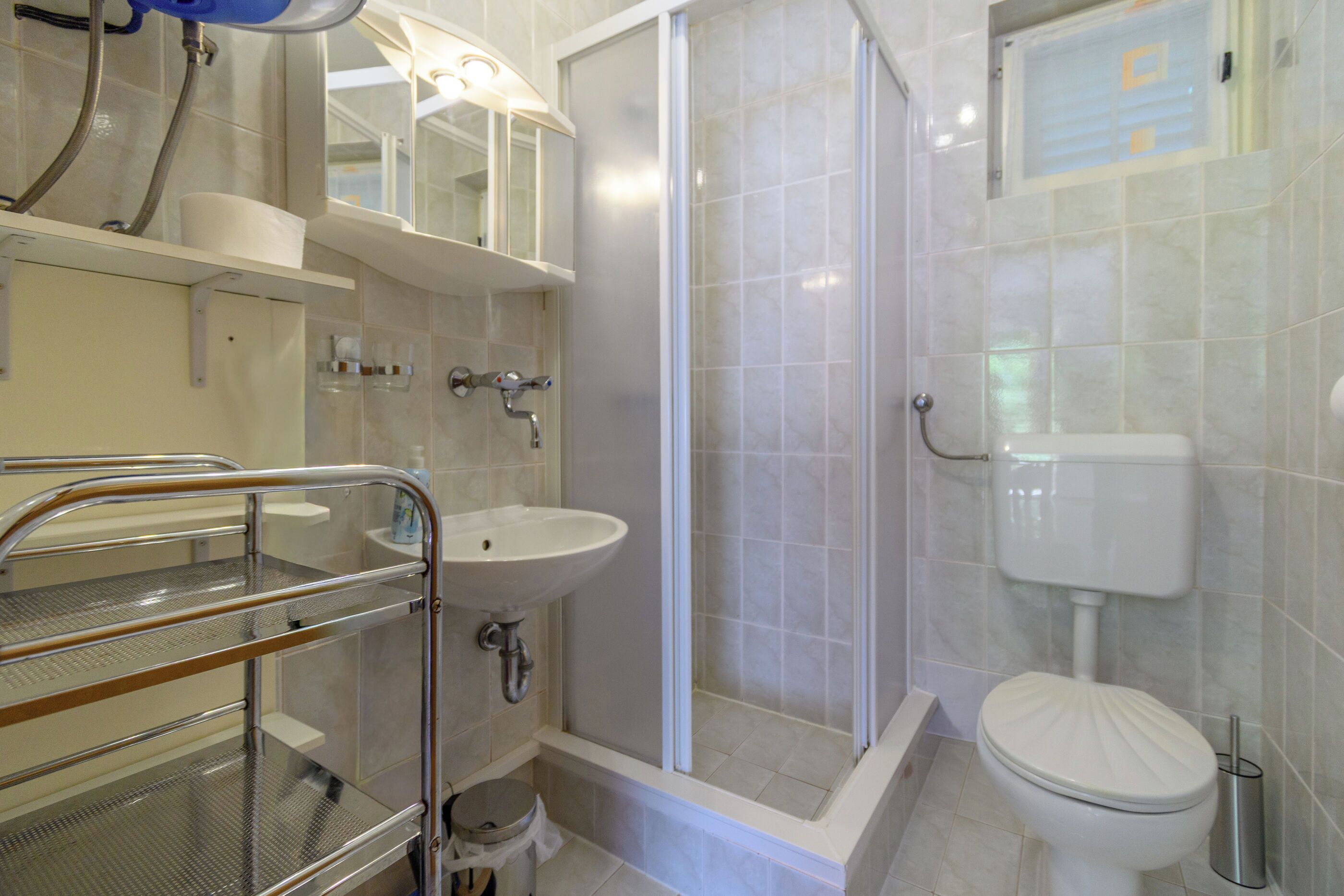 A bathroom with a shower, toilet, sink, and a metal shelf unit.