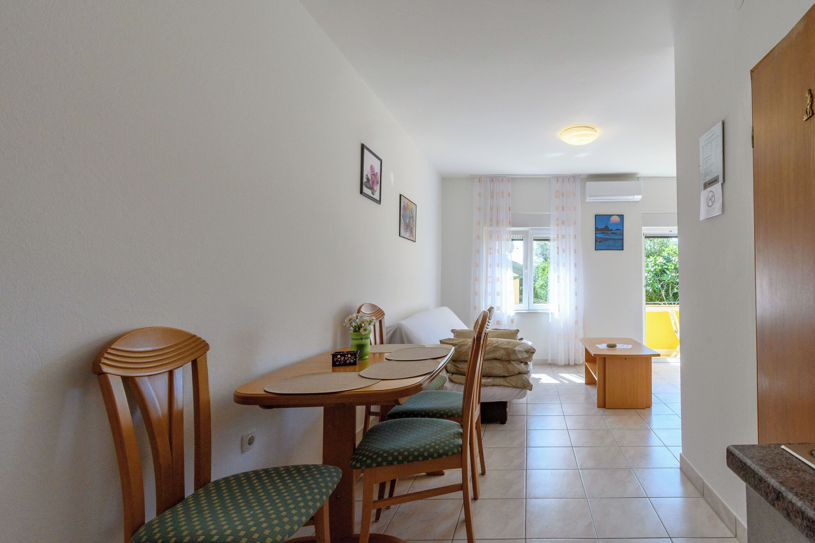 A dining area with a wooden table and chairs, a small side table, and a sofa in the background.