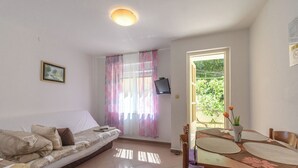 Una habitación con sofá, una mesa de comedor con individuales, televisor en la pared y ventana con cortinas.